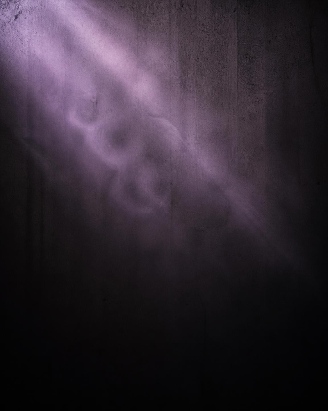 Dusty purple light beam drifting across a dark concrete wall